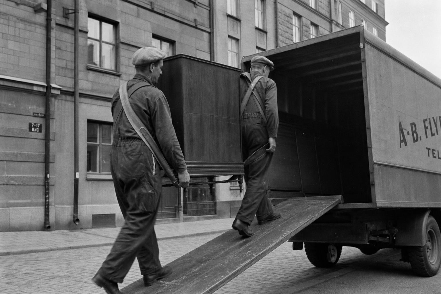 Flyttgubbar lastar en flyttbil från 1950-talet på en kullerstensgata i Göteborg